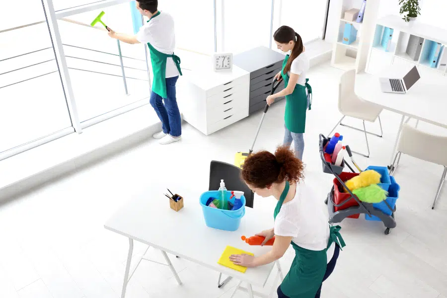 Three cleaners cleaning office windows, floor and desk